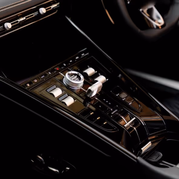 A detailed close-up of the Aston Martin DB12 Volante center console featuring metallic drive controls, luxury switchgear, glossy black trim, and premium interior craftsmanship.