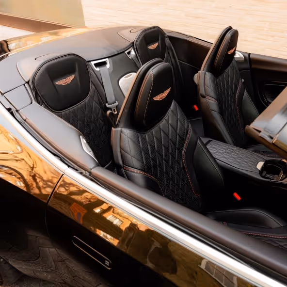 A high-angle interior shot of the Aston Martin DB12 Volante displaying the quilted leather seats, rear cabin area, center console, and elegant open-top configuration.