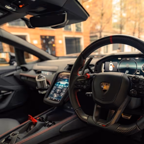 A high-end interior view of the Lamborghini Temerarioâs driver cockpit, featuring the carbon fiber steering wheel, digital dashboard, and red-trimmed center console.