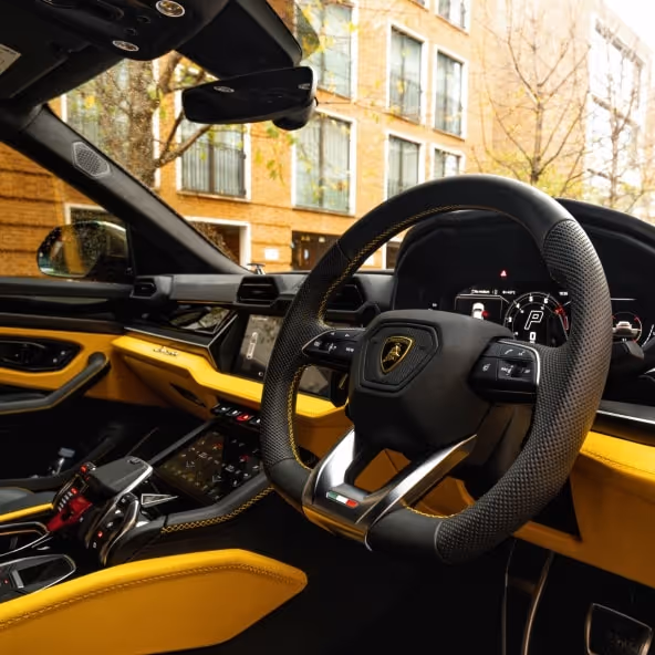 Front interior of a Lamborghini Urus showing the steering wheel and luxury cockpit design.