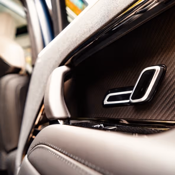 A detailed shot of the luxurious door panel, featuring glossy exposed carbon fibre trim that integrates seamlessly with the high-tech seat adjustment controls.