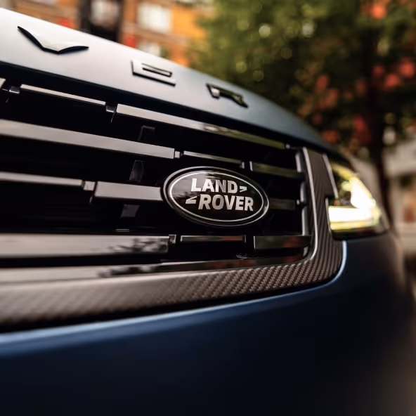 A distinctive close-up of the Land Rover badge centered above a bold carbon fibre grille section, highlighting the meticulous performance detailing on the SV model's front end.