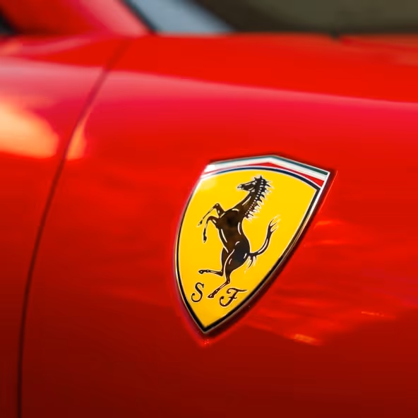 A macro close-up of the Ferrari prancing horse shield badge mounted on the red Ferrari Roma Spider bodywork, reflecting the luxury craftsmanship and iconic Italian branding.
