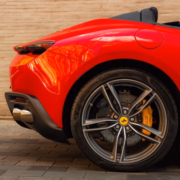 A detailed close-up of the Ferrari Roma Spider rear quarter panel featuring the black alloy wheel, yellow brake caliper, aerodynamic bodywork, and glossy red paint finish.