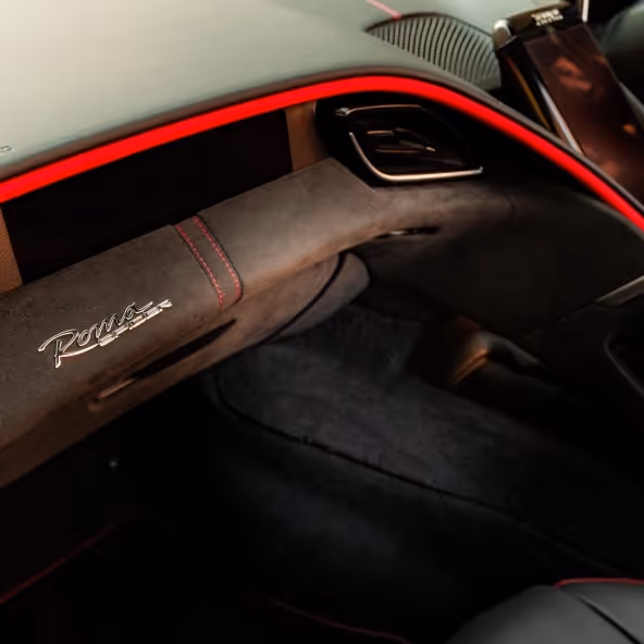 A close-up of the Ferrari Roma Spider passenger-side dashboard featuring premium leather upholstery, ambient red lighting, carbon fiber trim, and luxury Italian craftsmanship.