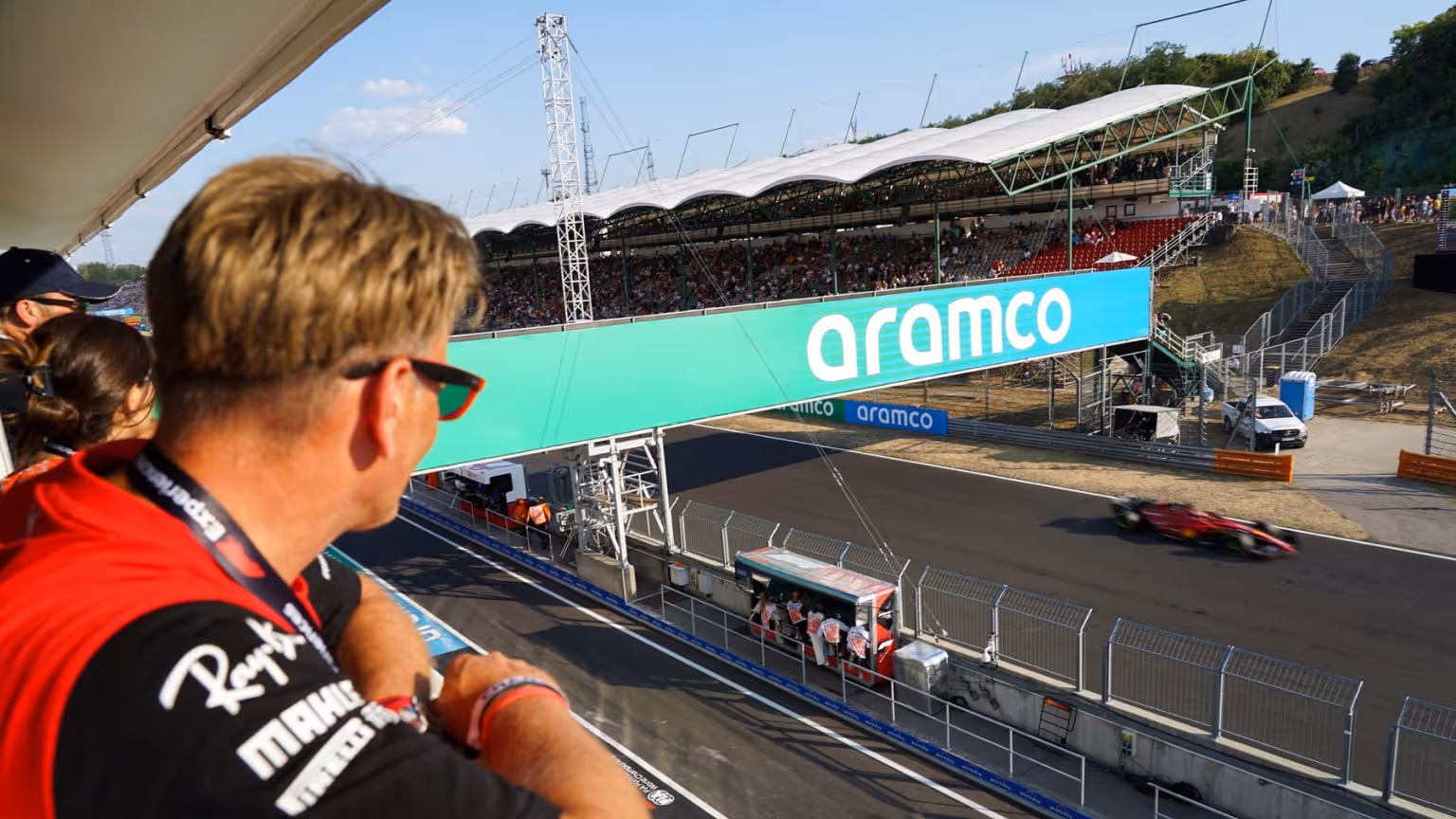 Guests enjoy premium trackside views from a hospitality suite overlooking the Melbourne Grand Prix circuit as a Formula 1 car speeds past below.
