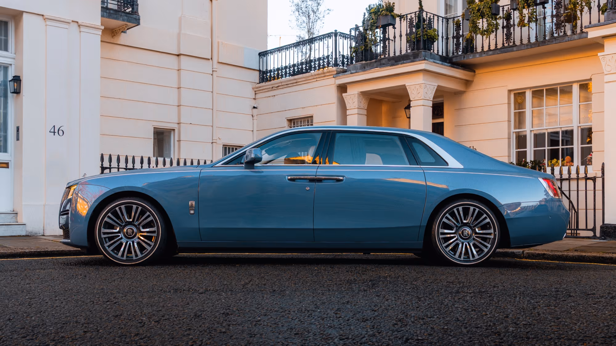 Side view of the LLC Rolls-Royce Ghost showcasing its long, commanding silhouette and high-gloss wheel detailing on a quiet, affluent London street.