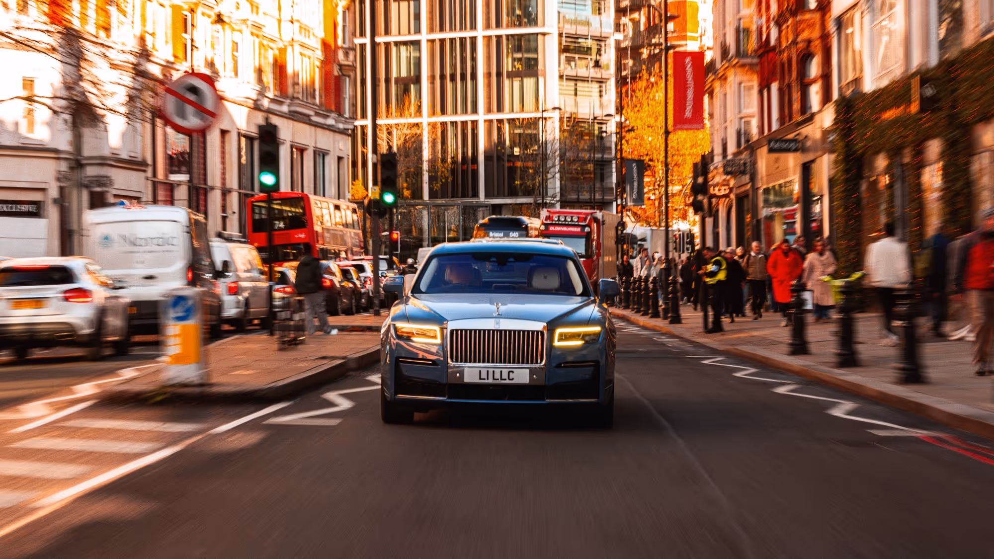 Front view of the Rolls-Royce Ghost navigating a busy central London thoroughfare, utilising motion blur to convey LLC's swift, fluent city mobility.