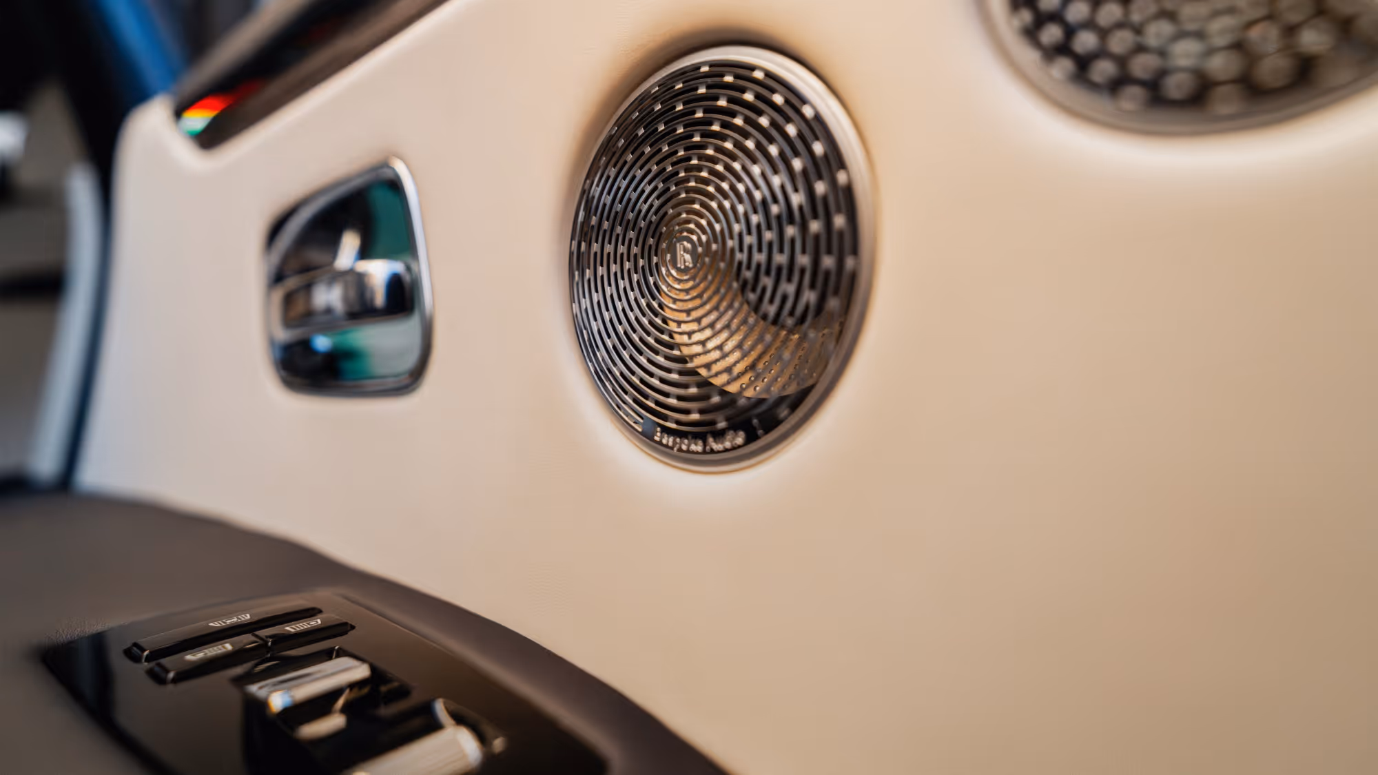Close-up of handcrafted Rolls-Royce Ghost rear cabin detailing, showcasing premium leather upholstery, polished metal finishes, and the bespoke speaker grille designed to enhance passenger comfort and luxury.