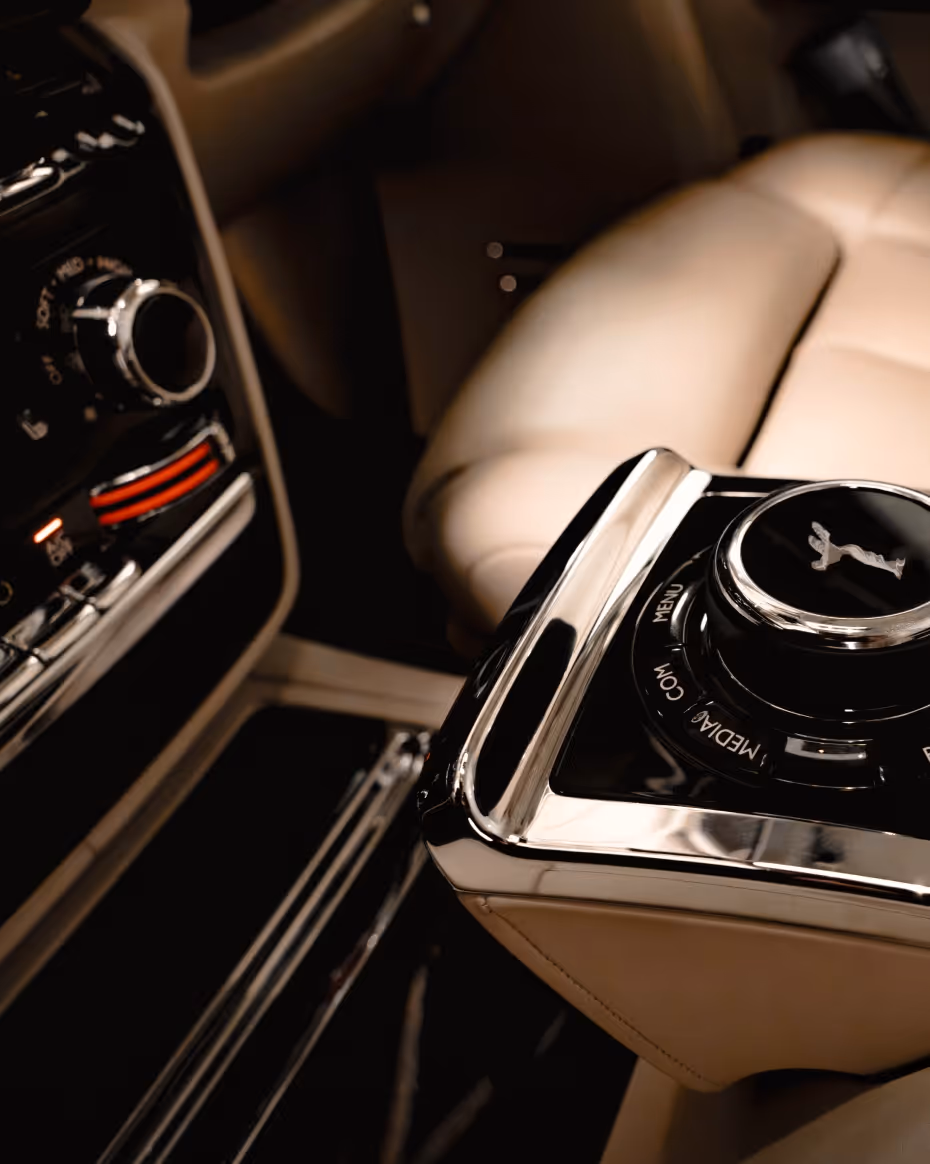 Close-up of the Rolls-Royce Phantom rear cabin control console, featuring premium leather upholstery, polished metal finishes, and executive passenger controls designed for first-class chauffeur travel.