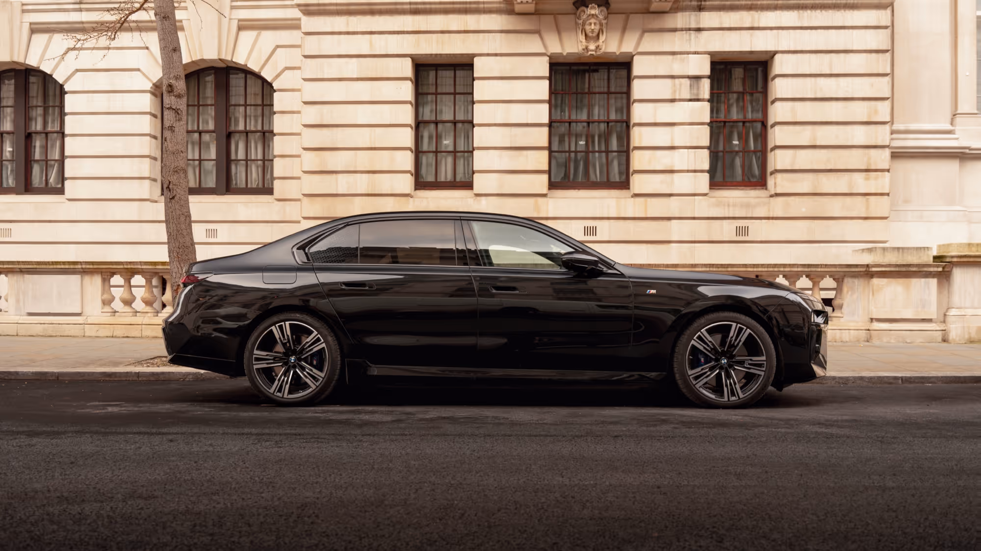 Side profile of a long-wheelbase BMW 7 Series chauffeur car with rear privacy glass.