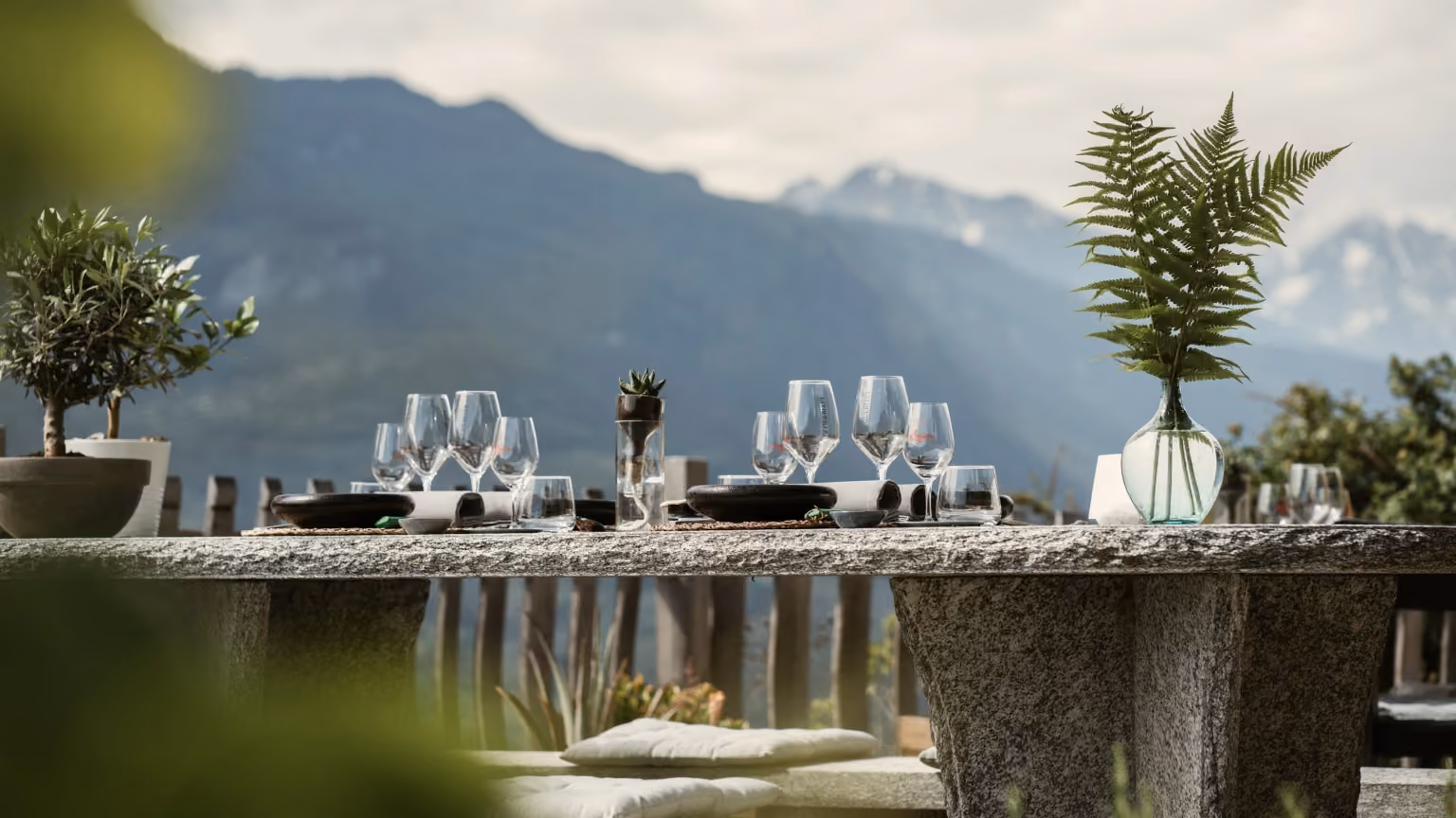 An outdoor dining table set with glassware and table settings overlooking mountains and a scenic natural landscape.