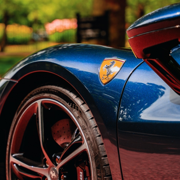 Close-up of the Ferrari 296GTB front fender featuring the Ferrari Shield badge, front wheel, brake caliper, and sculpted bodywork.