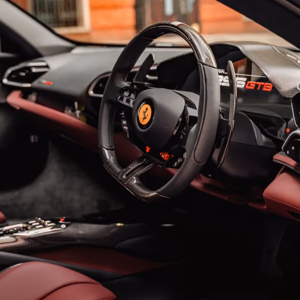 The driver’s cockpit of the Ferrari 296GTB featuring the signature steering wheel, digital instrument display, and premium leather-trimmed dashboard.