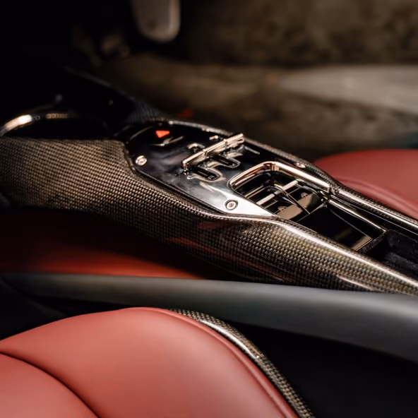 Close-up of the Ferrari 296GTB carbon-fibre centre console with metallic controls, gloss-black trim, and Rosso leather seats.