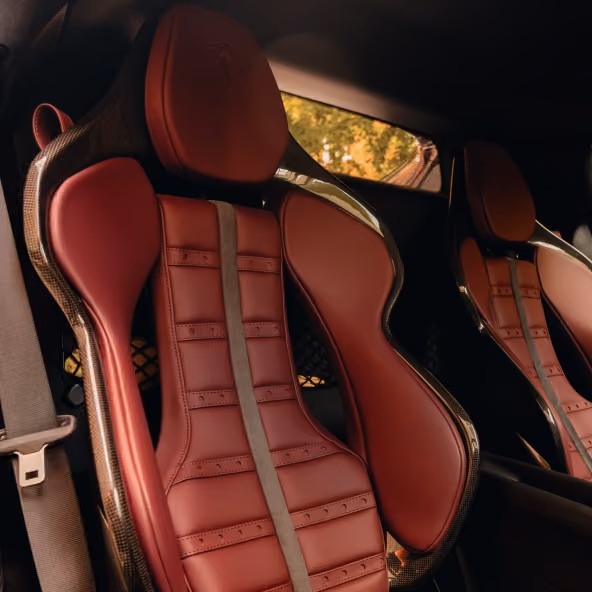 Interior view of the Ferrari 296GTB featuring Rosso leather sports seats with carbon-fibre seat shells, embossed Ferrari logos, and refined cabin craftsmanship.