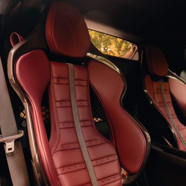 Interior view of the Ferrari 296GTB featuring Rosso leather sports seats with carbon-fibre seat shells, embossed Ferrari logos, and refined cabin craftsmanship.