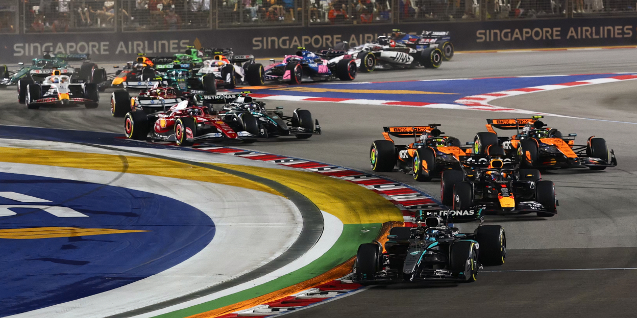 Multiple Formula 1 cars racing through a corner at the Marina Bay Street Circuit during the Singapore Grand Prix with spectators in the grandstands.
