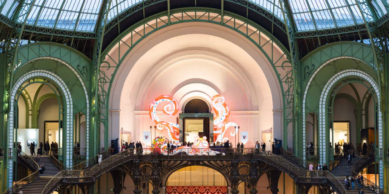 Interior of the Grand Palais during Art Basel Paris, with visitors gathered around contemporary art installations beneath the venue’s glass-and-iron structure.