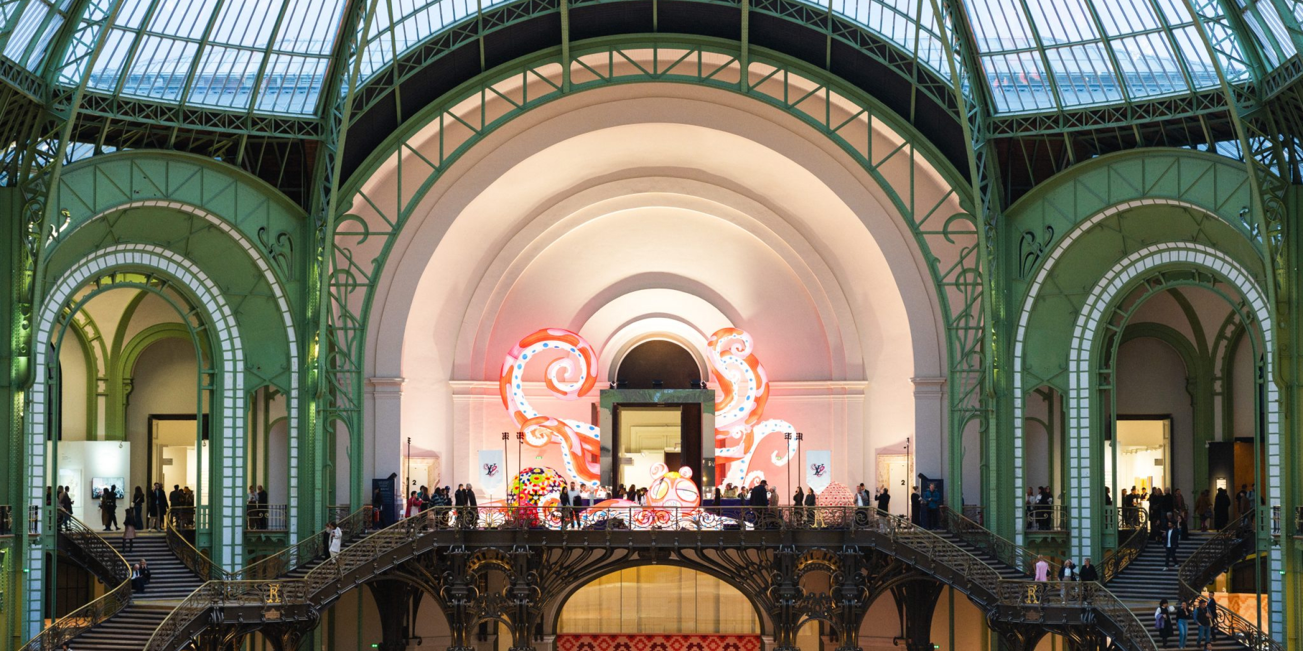 Interior of the Grand Palais during Art Basel Paris, with visitors gathered around contemporary art installations beneath the venue’s glass-and-iron structure.