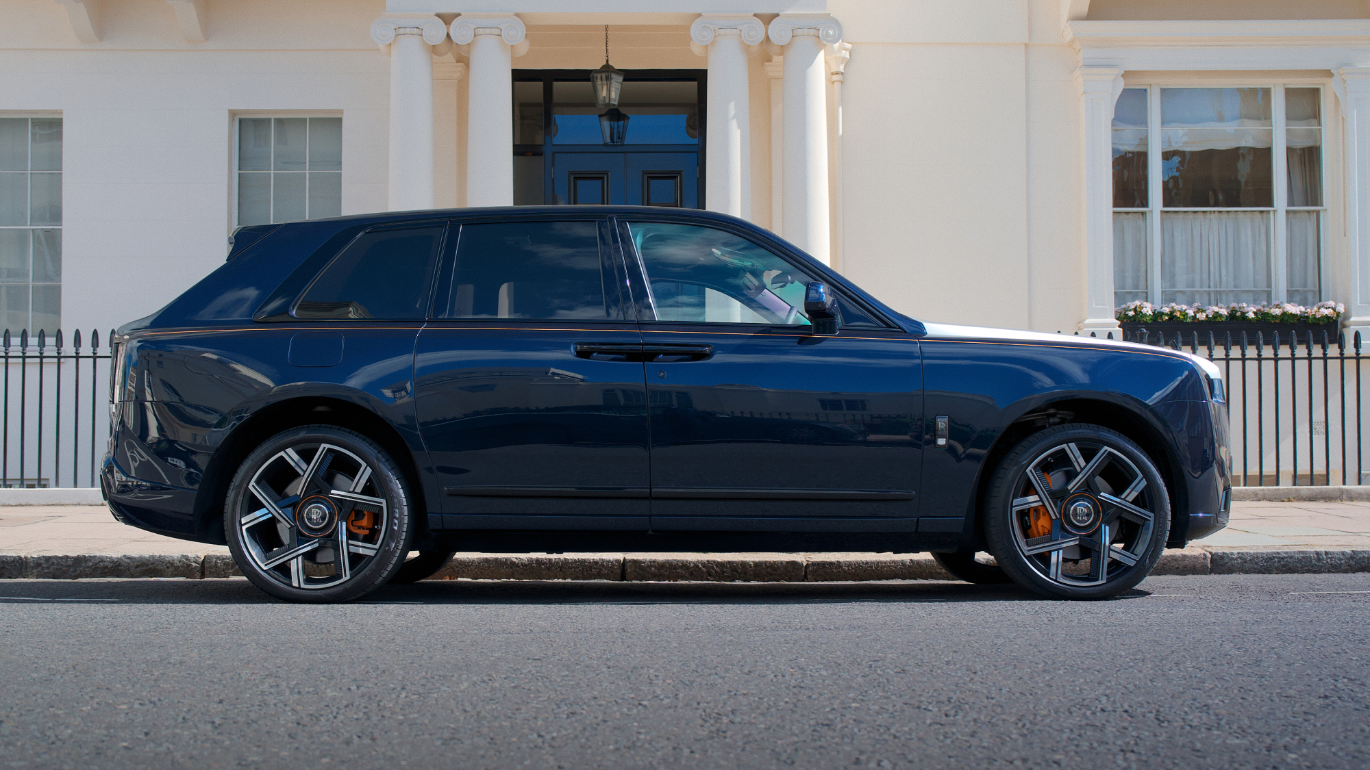 Side view of a Rolls-Royce Cullinan parked on a London street, highlighting its full-size luxury SUV proportions and distinctive profile.