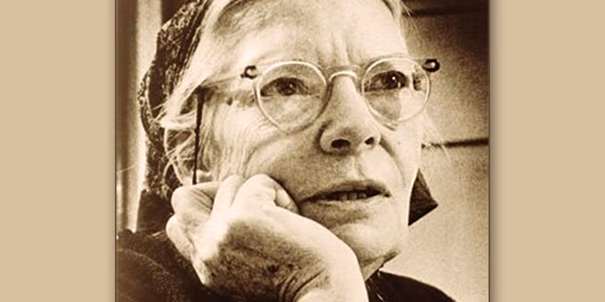 Sepia photo of an elderly woman wearing glasses and a headscarf, resting her chin on her hand.