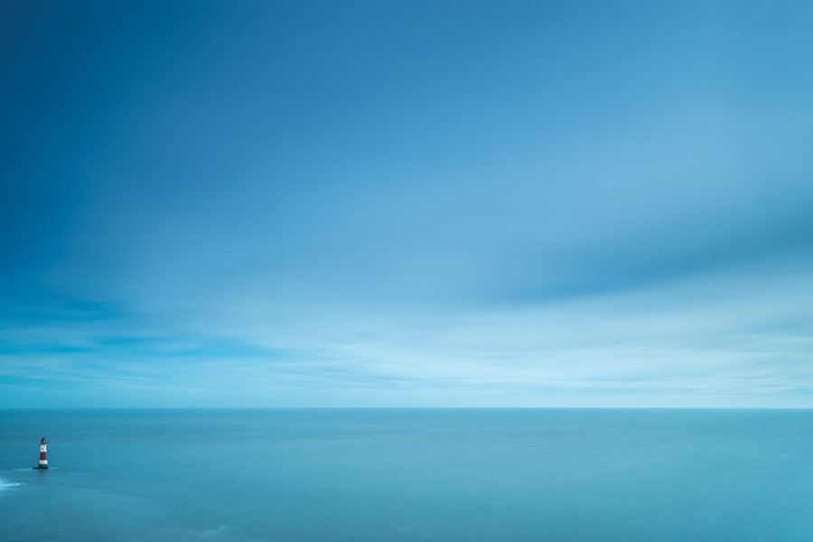 tiny lighthouse by huge sea and sky