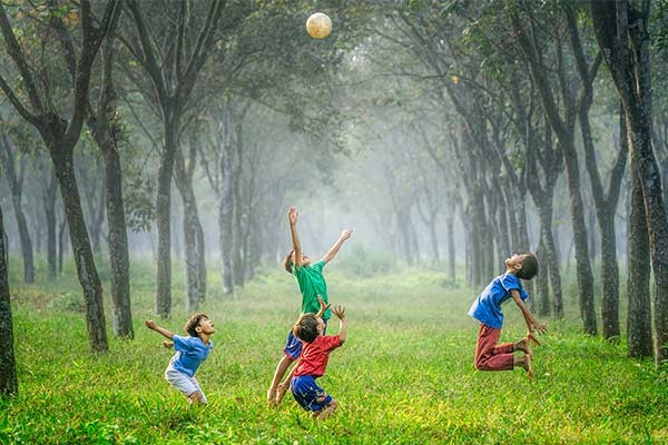 four boys jumping to hit a soccer ball in a forest