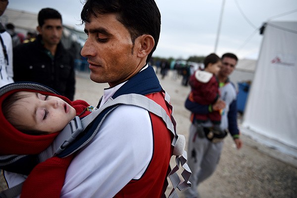  refugee man carries his child inside the makeshift refugee camp of Idomeni in norhern Greece.