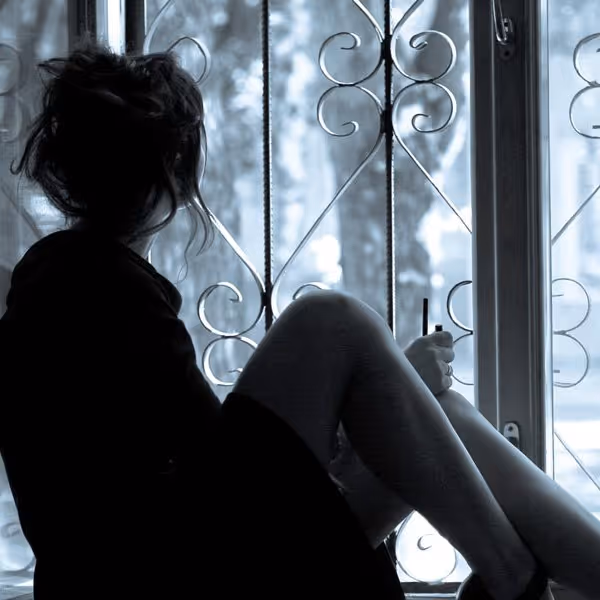 Silhouette of a person sitting by a window with decorative bars, holding a vape pen.