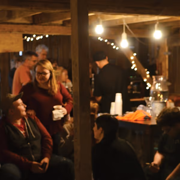 Group of people socializing inside a warmly lit rustic wooden room with string lights and hanging bulbs.