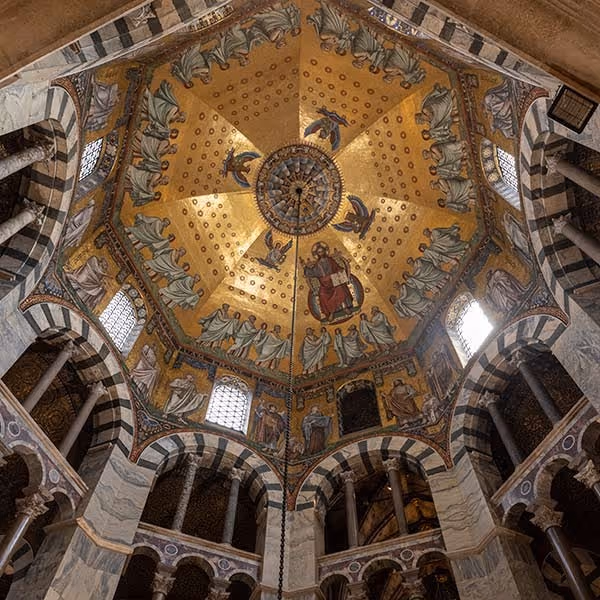 Ornate cathedral dome with gold mosaic of religious figures and striped marble arches below.