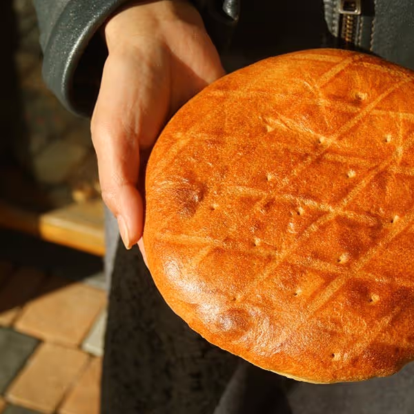 Hand holding a round loaf of golden-brown bread with a crisscross pattern on top.