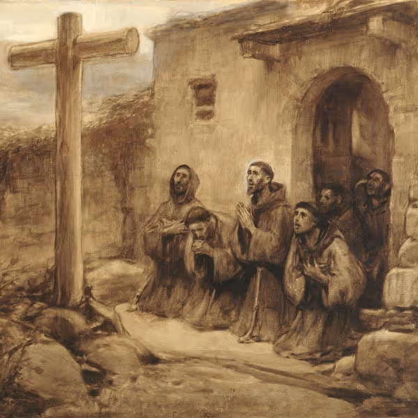 A group of friars in brown robes kneeling and praying near a large wooden cross by a stone building.