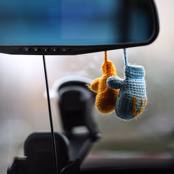 Miniature knitted boxing gloves, one blue and one orange, hanging from a car's rearview mirror.