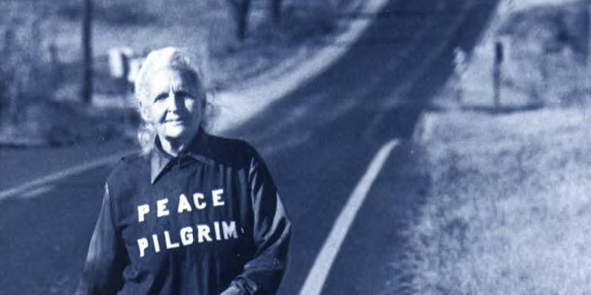 Older woman walking on a country road wearing a shirt that says Peace Pilgrim.