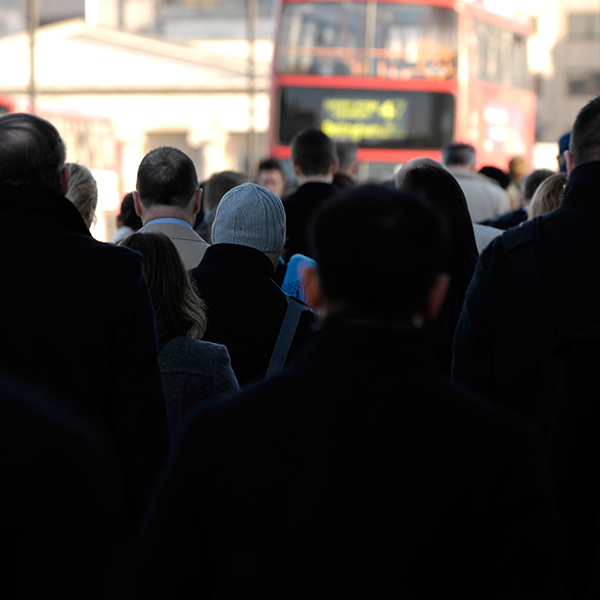 Crowd of people walking with a red double-decker bus in the blurred background.