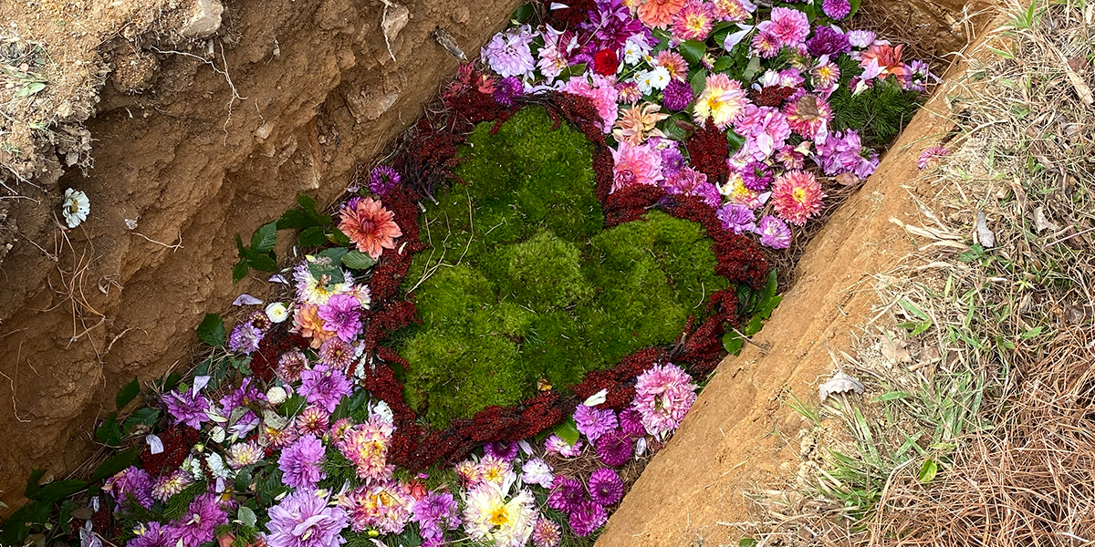Close-up of a grave with colorful flowers and a heart-shaped patch of green moss inside the earth.