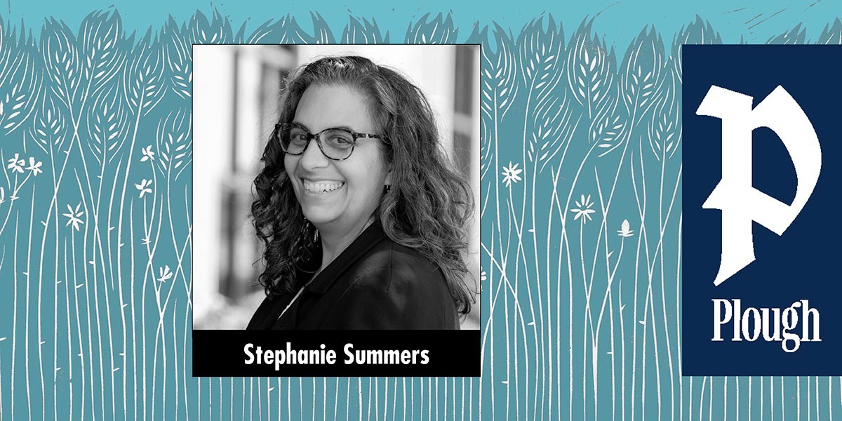 Black and white portrait of Stephanie Summers smiling, wearing glasses and a dark jacket.
