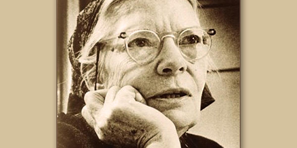 Black and white close-up portrait of an elderly woman wearing glasses and a headscarf, resting her chin on her hand.