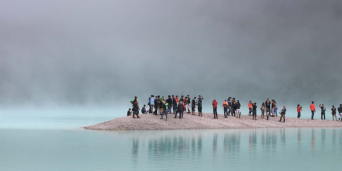Group of people gathered on a small rocky island surrounded by mist and calm blue-green water.
