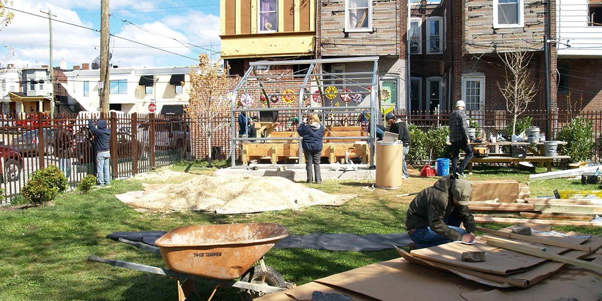 People working on a garden project with wooden structures and tools in a fenced urban yard.