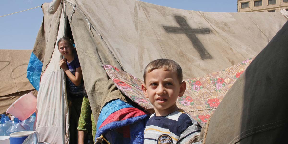 Boy and girl near a tent with a cross symbol, surrounded by containers and fabric quilts.