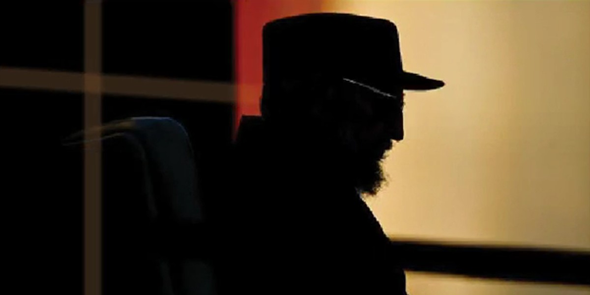Silhouette of a man with a beard and hat sitting, with a dark and orange background.