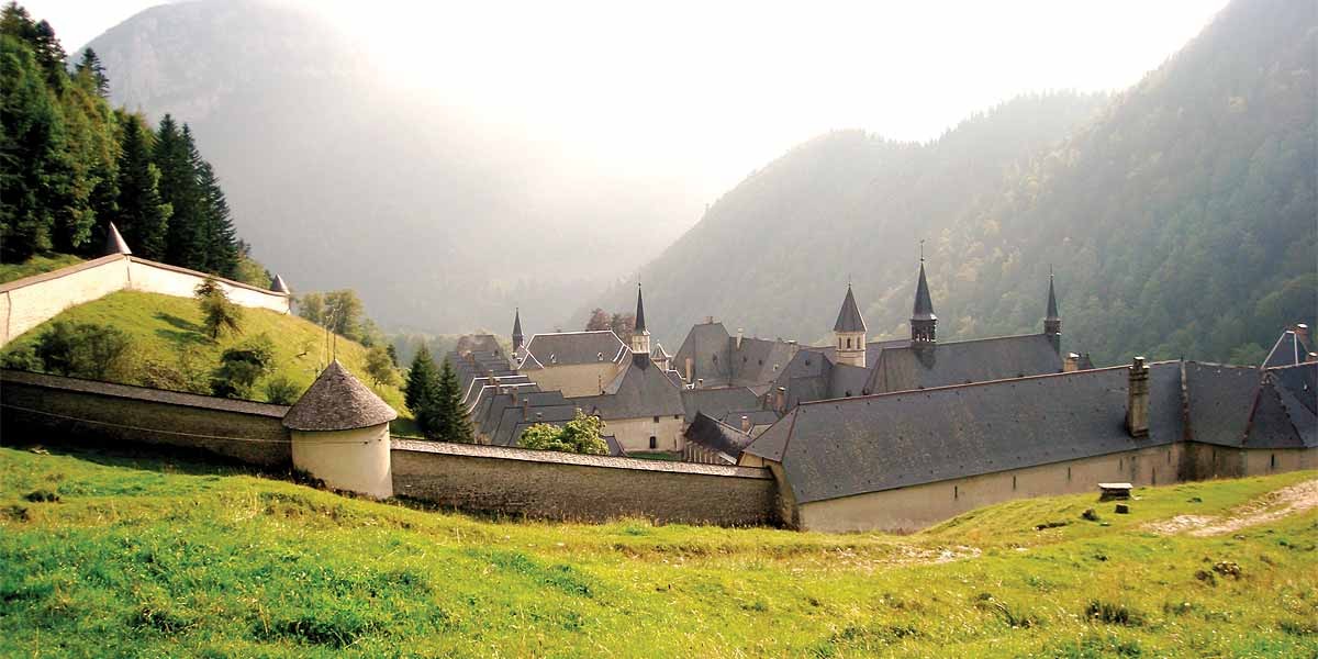 Historic monastery buildings with slate roofs and towers surrounded by green hills and misty mountains.