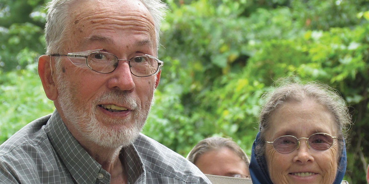 Smiling elderly man and woman outdoors with green foliage background.