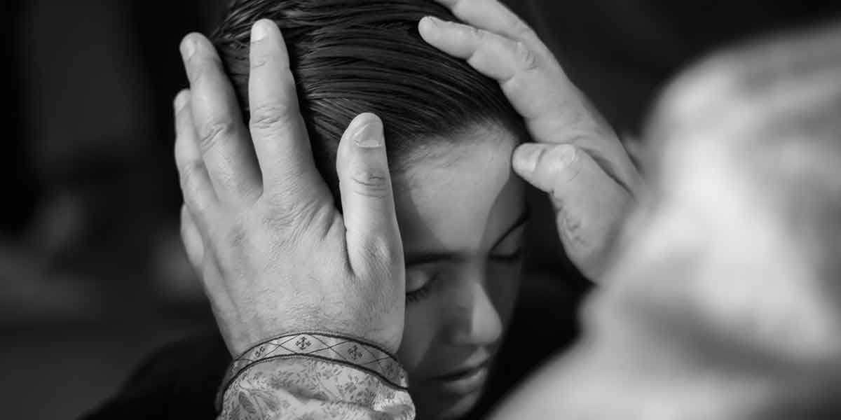 Black and white image of hands gently holding a woman's head with her eyes closed.