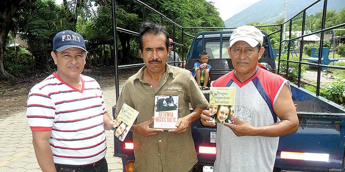 Three men standing in front of a truck, holding books or pamphlets with messages in Spanish.