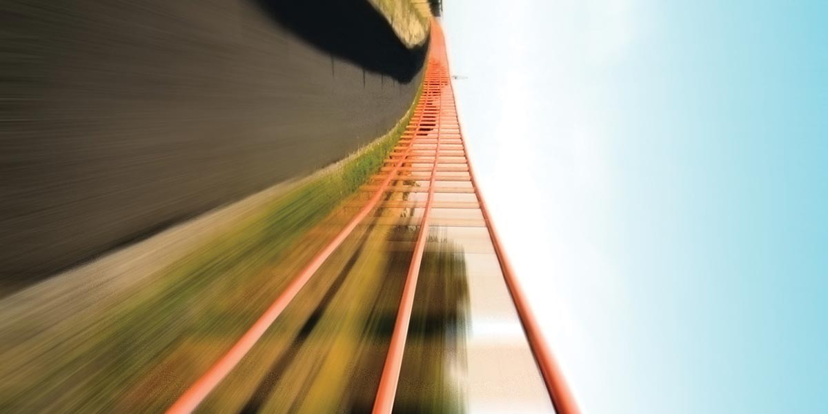 Blurred motion view of a red railroad track curving upward against a blue sky background.