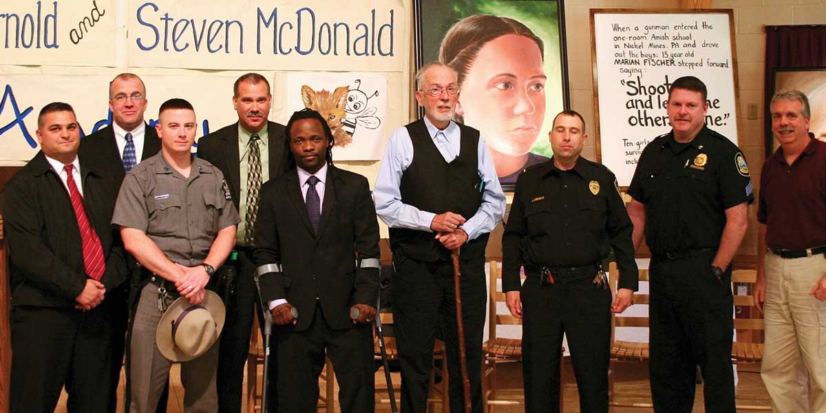 Group of men including police officers and a man with a cane standing in front of posters and a painting.